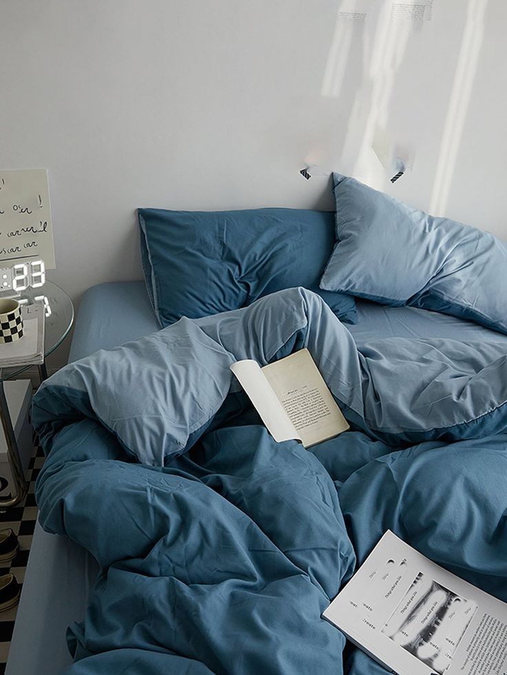 an unmade bed with blue sheets and pillows on it in a room that has black and white checkered flooring