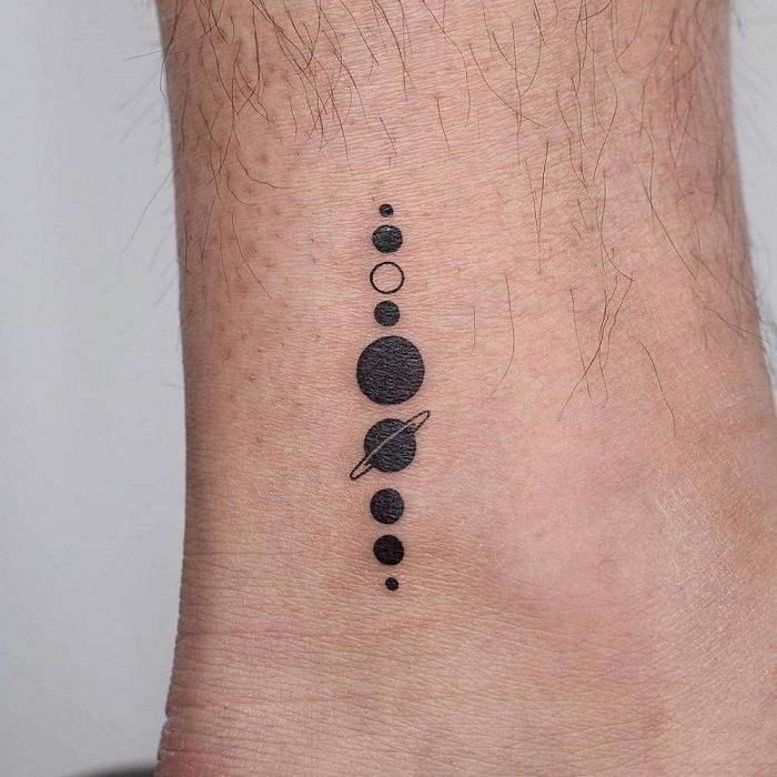 a black and white photo of a small tattoo on the ankle that has planets in it