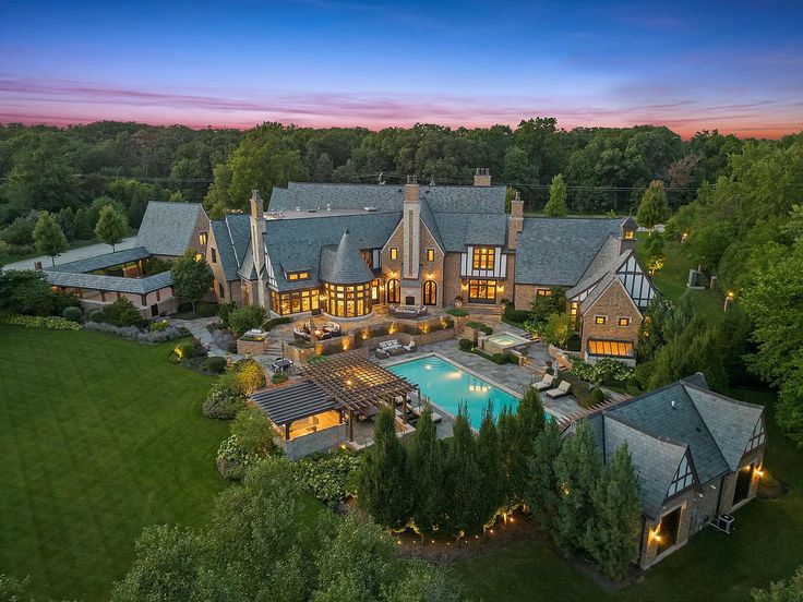 an aerial view of a large home with a swimming pool in the foreground and lots of trees surrounding it