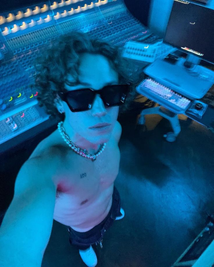 a man wearing sunglasses sitting in front of sound mixing equipment with his hand on his hip