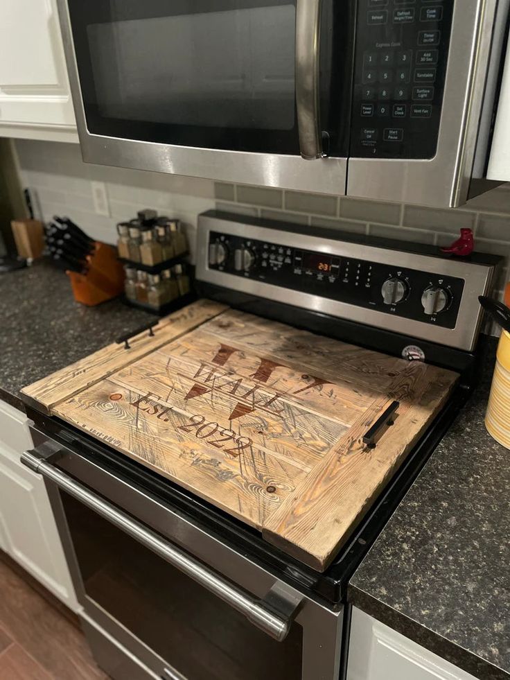 a wooden cutting board sitting on top of an oven in a kitchen next to a microwave