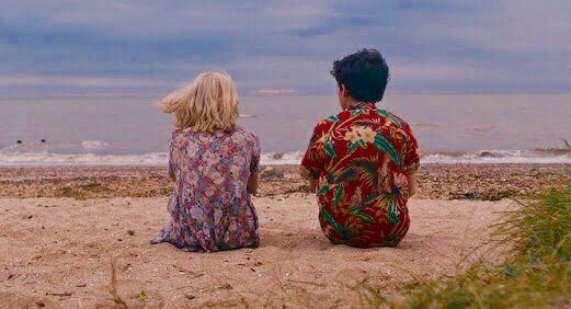 two people sitting on the beach looking out at the water