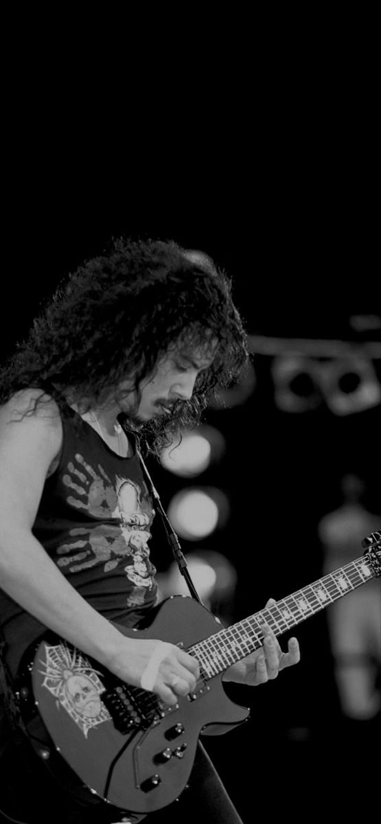 a black and white photo of a man with long curly hair playing an electric guitar