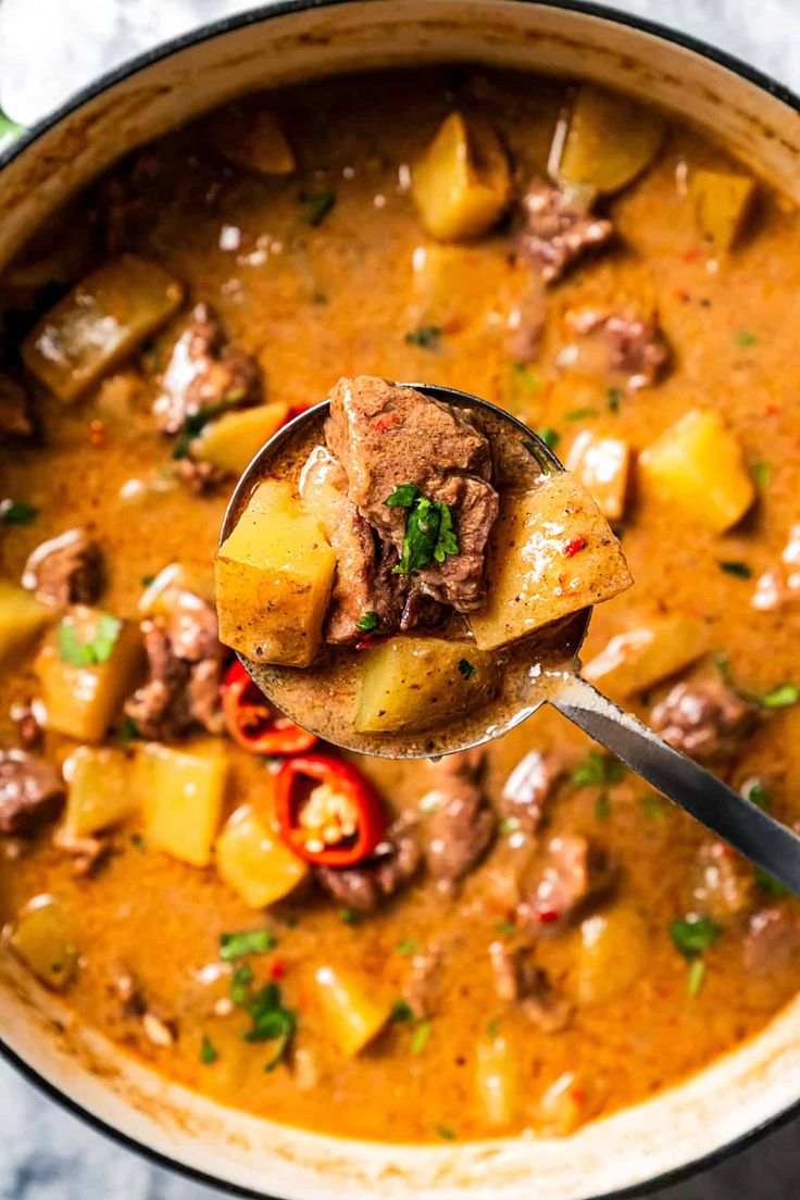 a ladle full of stew with meat and vegetables in it, ready to be eaten