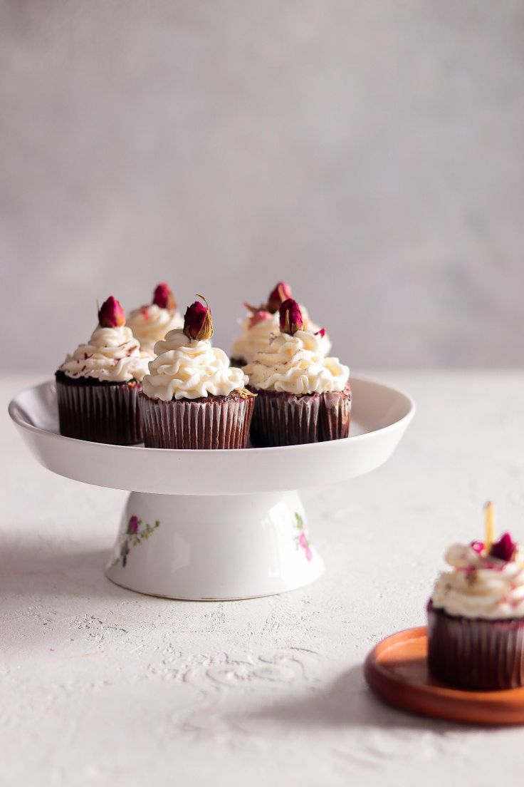 cupcakes with white frosting and raspberries on top sitting on a cake plate