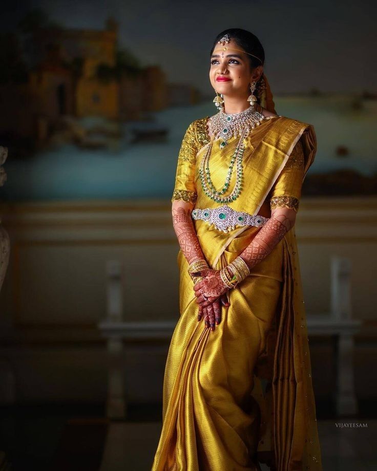 a woman in a yellow sari and jewelry poses for the camera with her hands on her hips