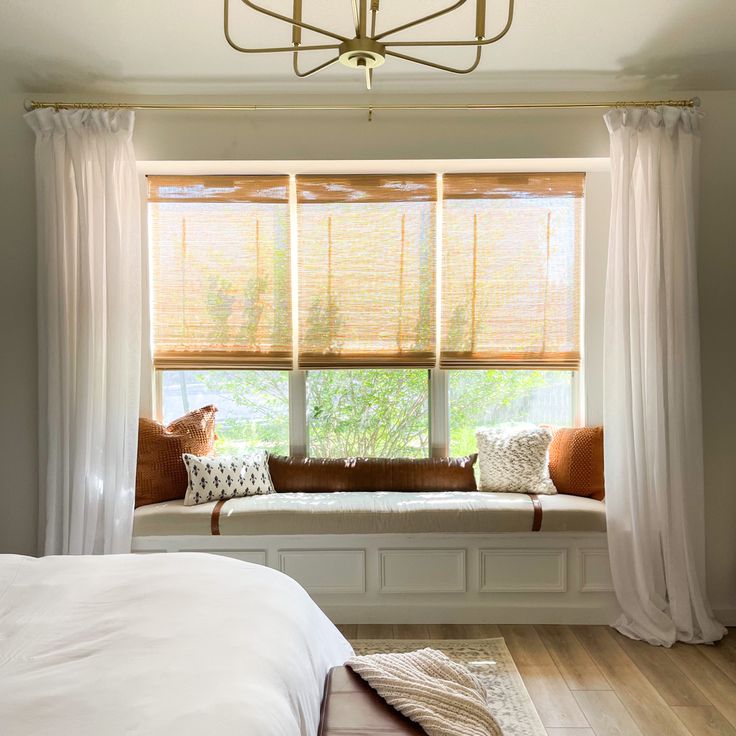 a bedroom with a large window seat next to a white bed and wooden flooring