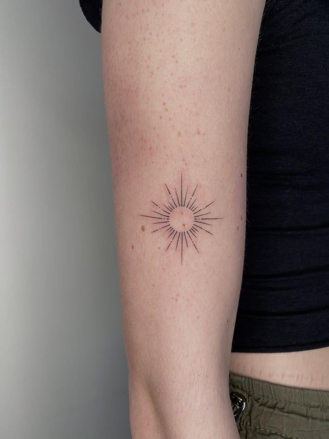 a woman's arm with a small sun tattoo on the left side of her arm