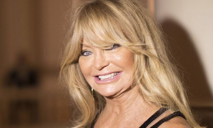 a woman with blonde hair and blue eyes smiles at the camera while wearing a black dress