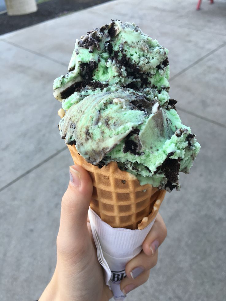 someone holding up an ice cream cone with chocolate chip cookies and oreo chunks on top