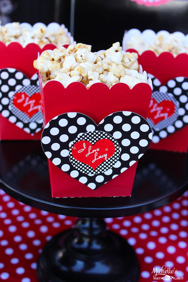 three red boxes filled with popcorn sitting on top of a black cake platter covered in polka dots