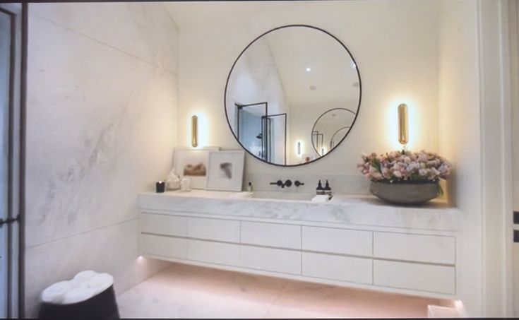 a bathroom with a large round mirror above the sink and lights on the wall behind it