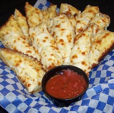 some pizza sticks are on a blue and white checkered paper with a small bowl of sauce