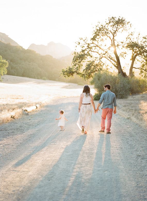 a man and woman walking down a dirt road next to a small child holding hands