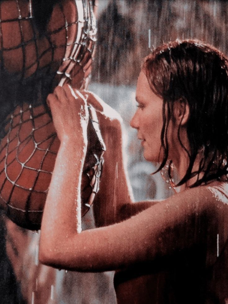 a woman in the rain holding up a spider - man mask to her face with water coming out of it