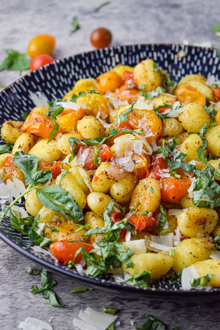 a bowl filled with potatoes and vegetables on top of a table next to some tomatoes