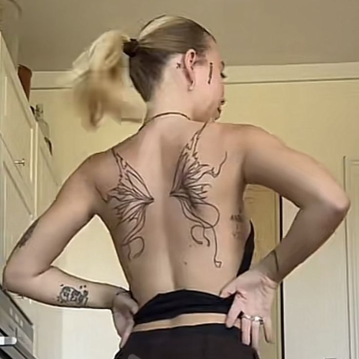 a woman with tattoos on her back standing in a kitchen