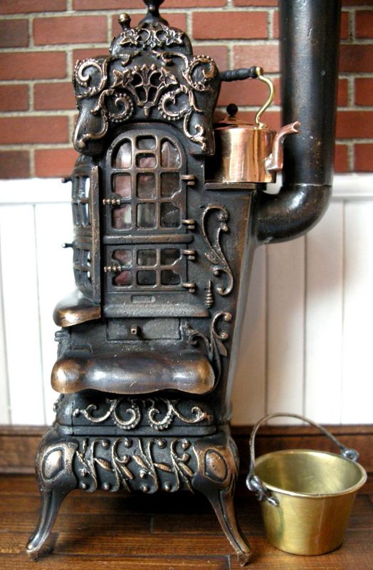 an old fashioned stove sitting on top of a wooden floor next to a bucket and a brick wall