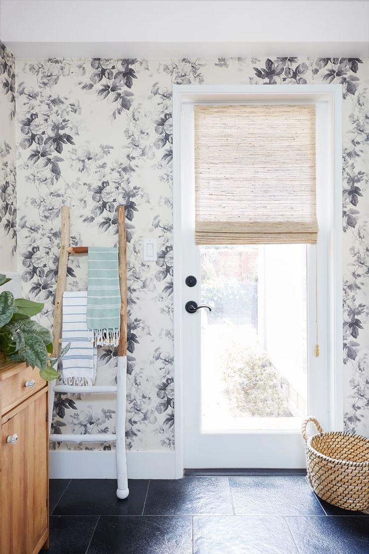 a white door in front of a floral wallpapered room with a basket and towel rack