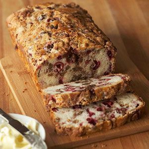 a loaf of fruit bread sitting on top of a wooden cutting board next to butter