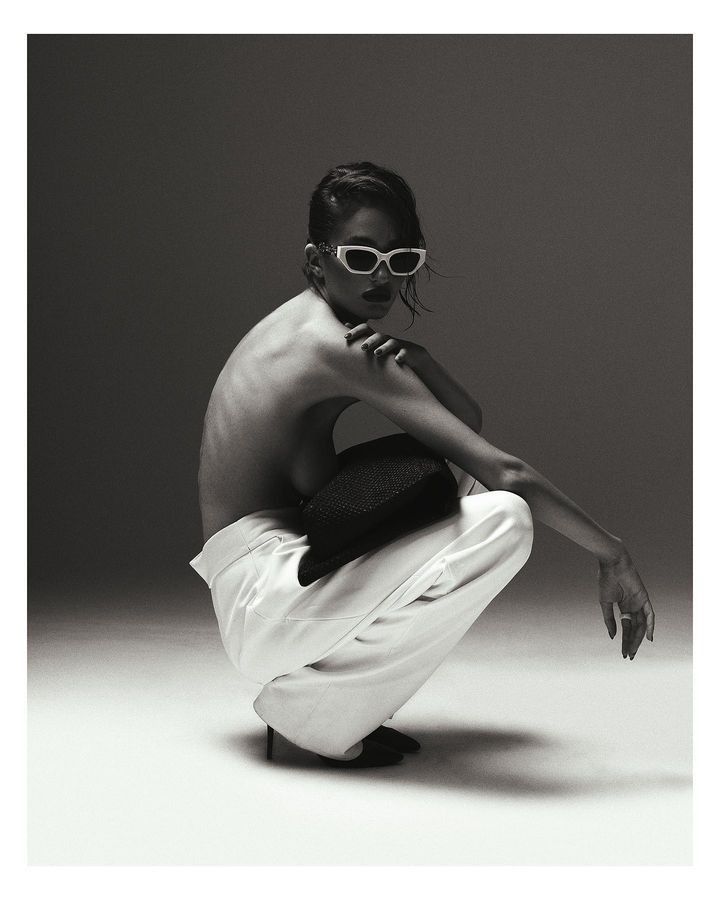 a black and white photo of a shirtless woman with sunglasses sitting on the ground