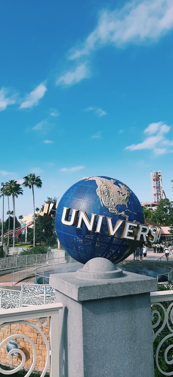 a large blue and gold globe sitting on top of a cement pillar in front of palm trees