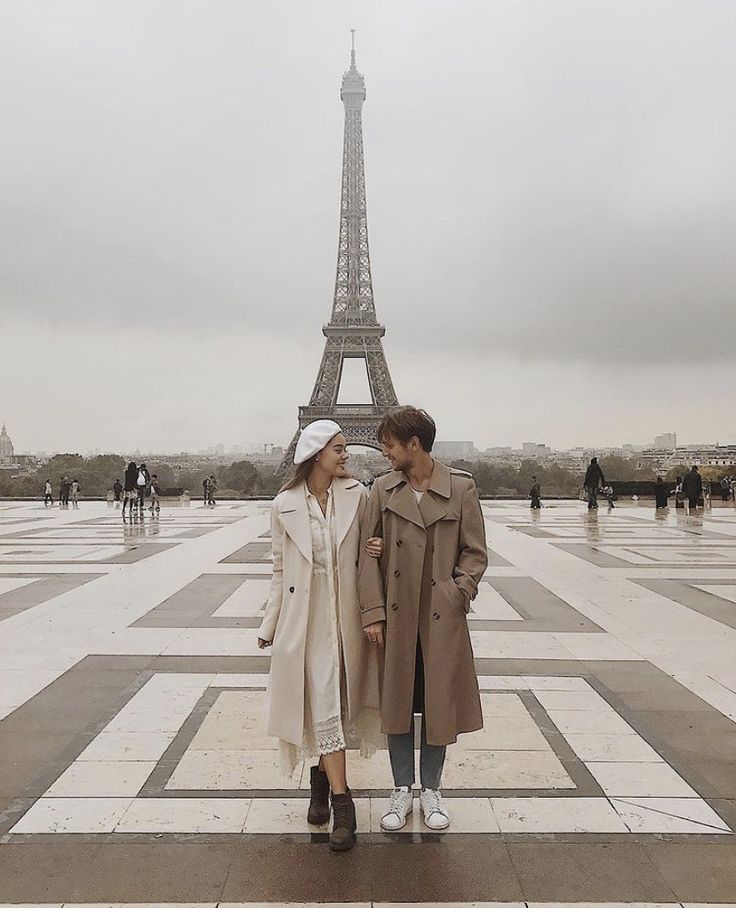 two people standing next to each other in front of the eiffel tower on a cloudy day