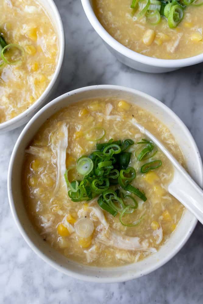 three white bowls filled with soup on top of a marble counter topped with green onions