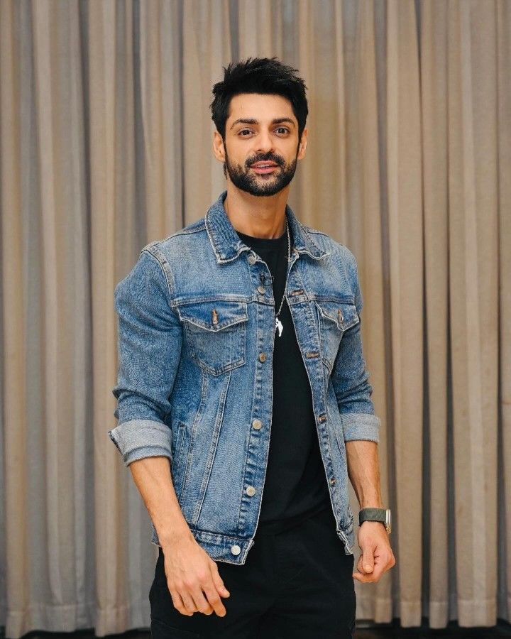 a man standing in front of a curtain wearing a denim jacket and black t - shirt