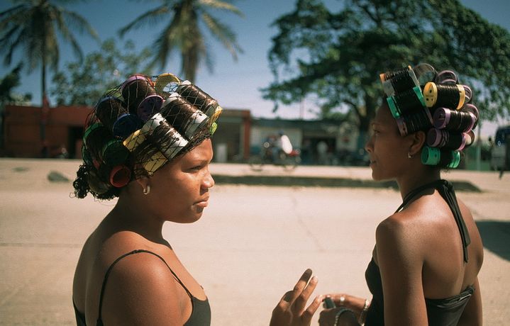 two women standing next to each other with hair clips on their head and one holding a cell phone