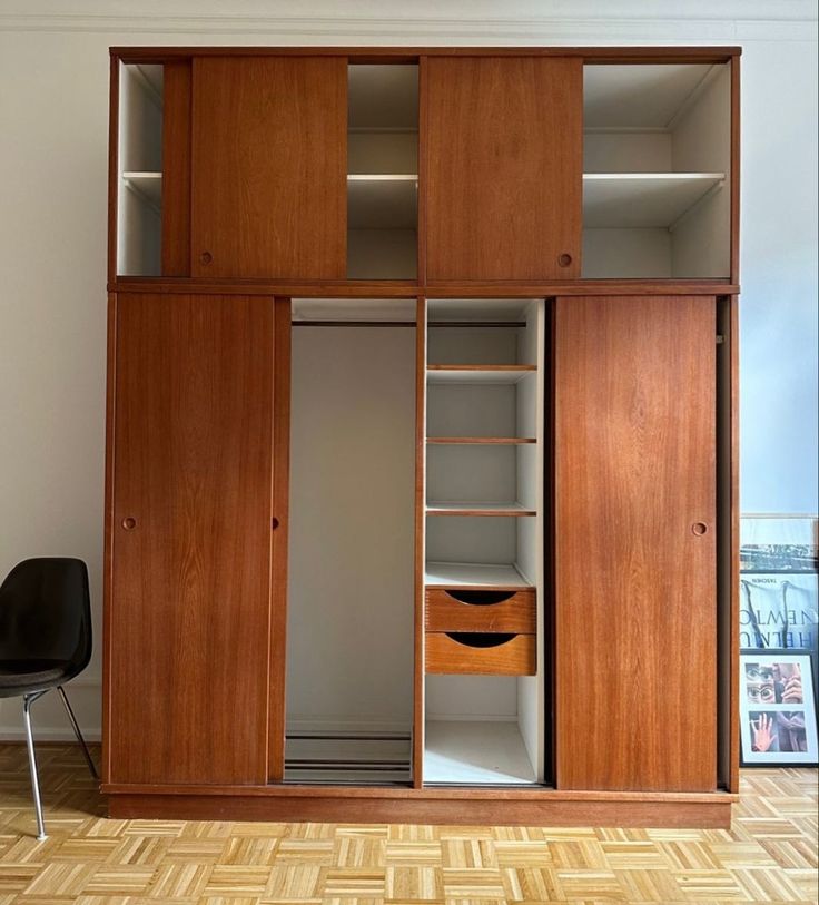 an empty closet with wooden shelves and drawers in the corner, next to a black chair