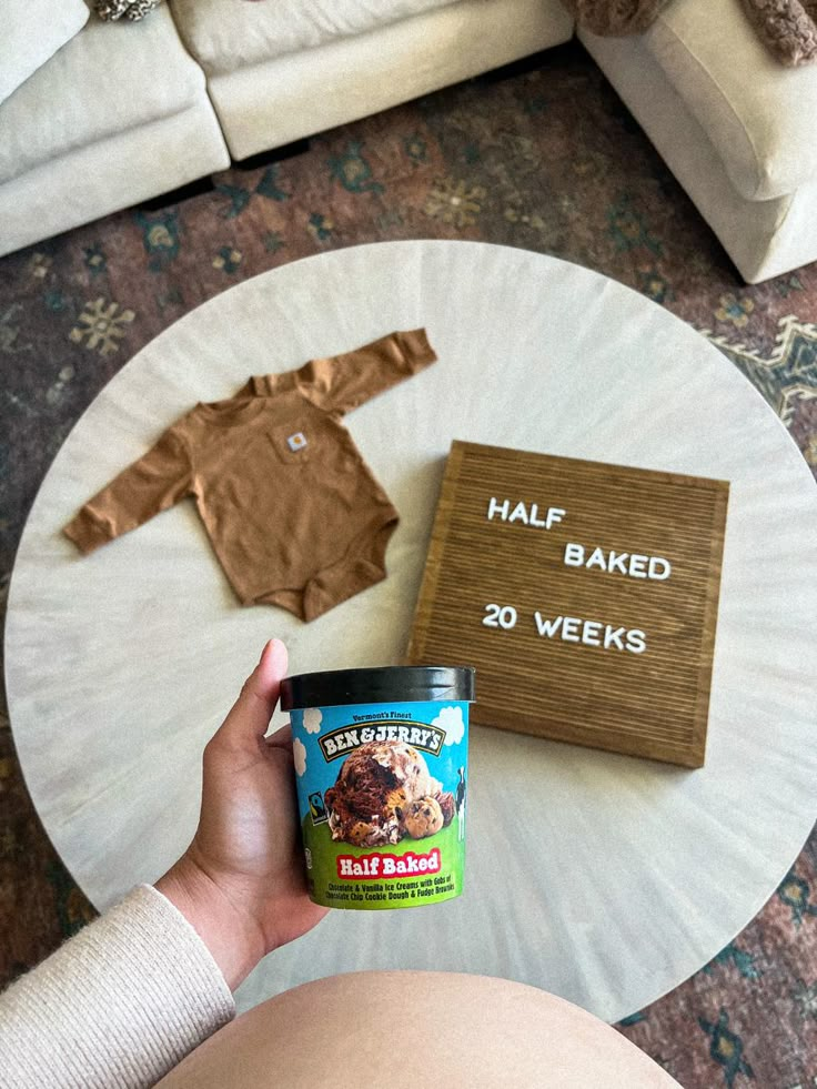 a person holding a jar of ice cream next to a baby's bodysuit