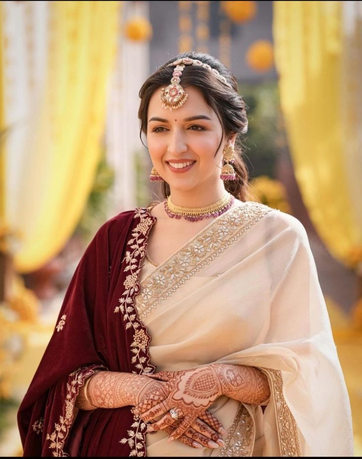 a woman in a white and maroon sari with her hands on her chest, smiling at the camera