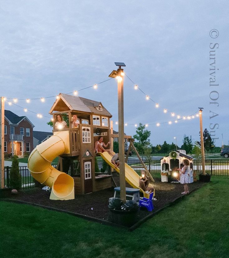 children are playing in the backyard with lights strung over them and a play structure that has a slide