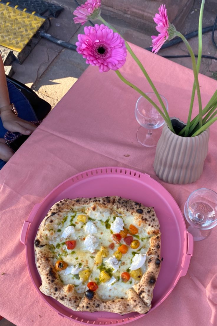 a pizza sitting on top of a pink plate next to a vase filled with flowers