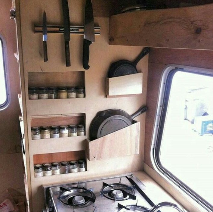 a stove top oven sitting inside of a kitchen next to two open windows with pots and pans hanging on the wall