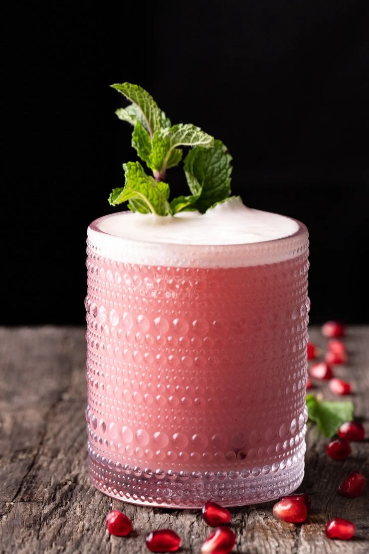 a pink drink with mint and pomegranate garnishes on a wooden table