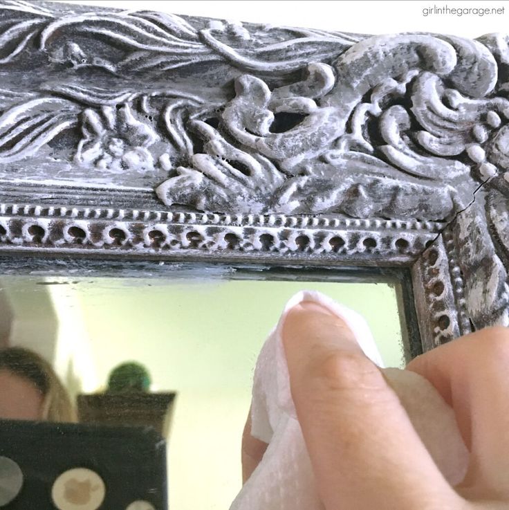 a person is cleaning their hand with a cloth in front of a silver framed mirror