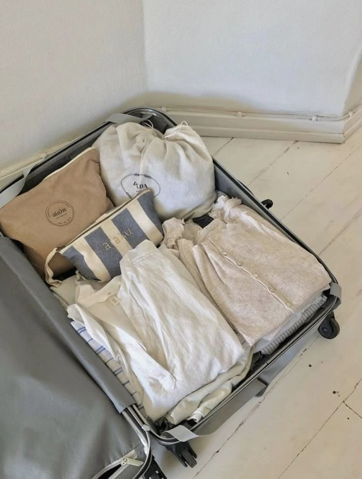 an open suitcase filled with clothes on top of a hard wood floor next to a wall