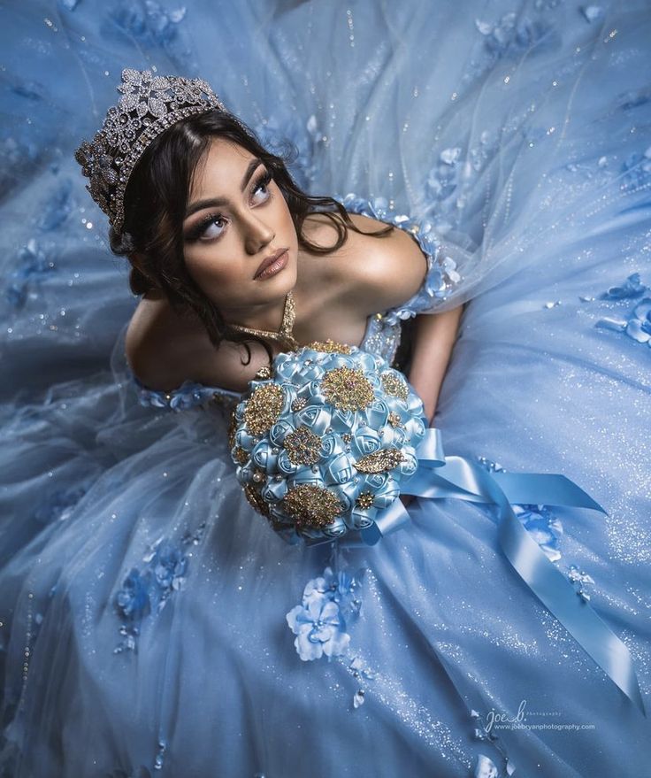 a woman in a blue dress with a tiara on her head is holding a bridal bouquet