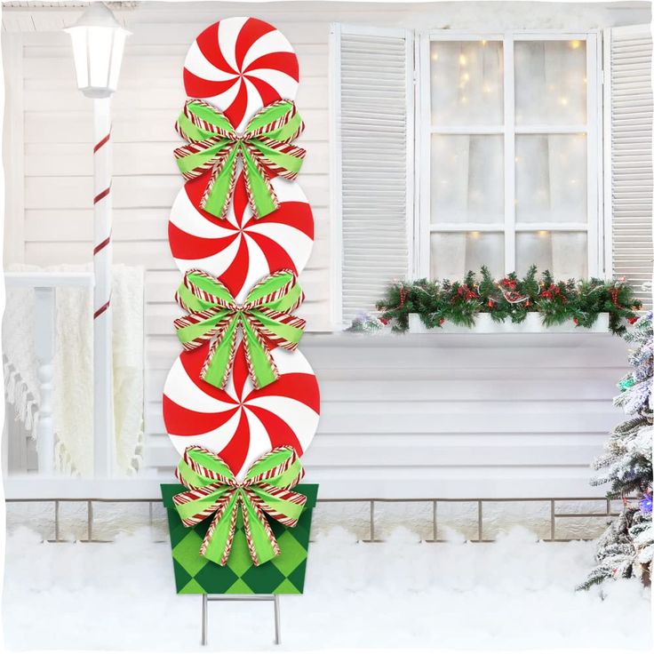 two candy canes in the snow next to a christmas tree and porch with holiday decorations