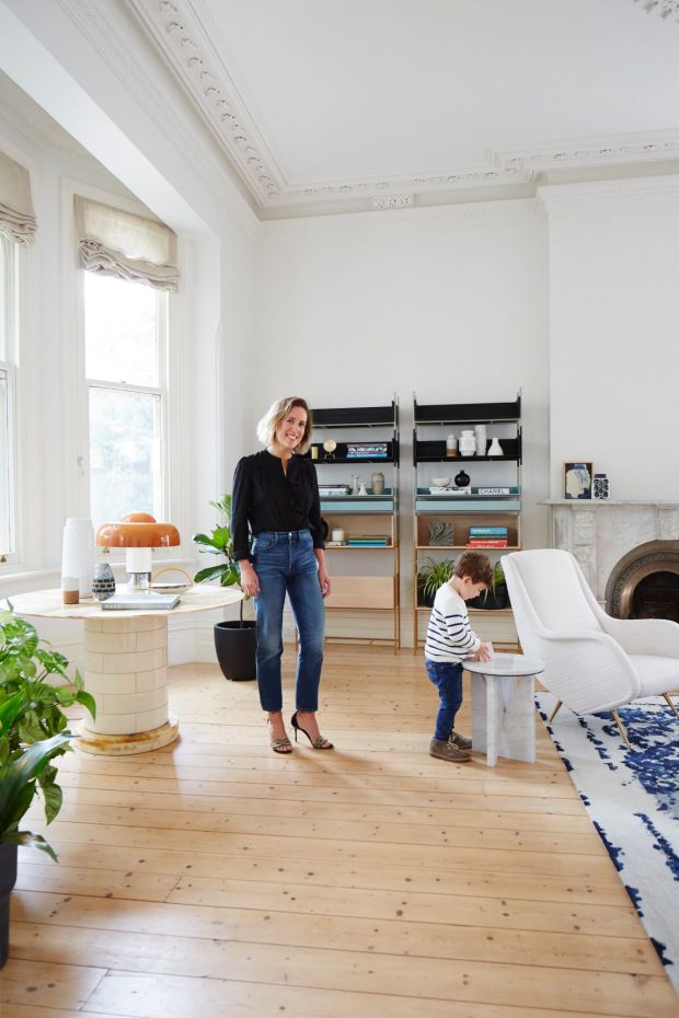 a woman standing next to a child in a living room filled with furniture and plants