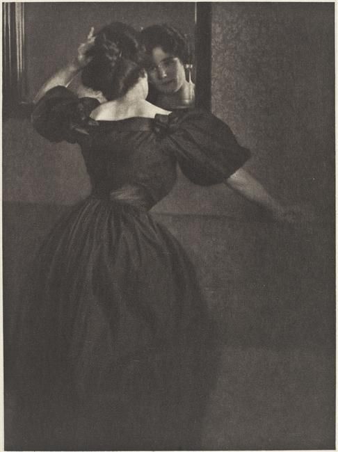 an old photo of a woman standing in front of a mirror looking at herself in the mirror