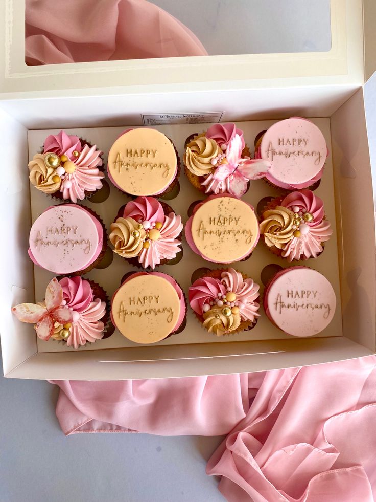 a box filled with cupcakes covered in pink frosting and gold icing