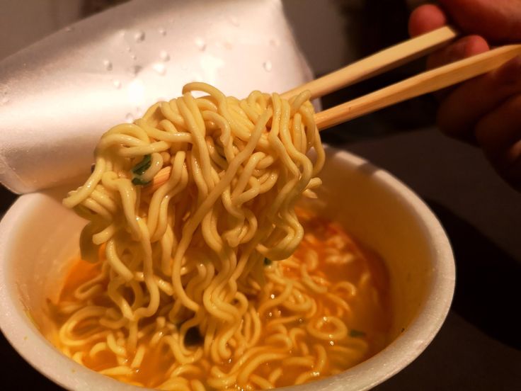 someone is holding chopsticks over a bowl of noodles