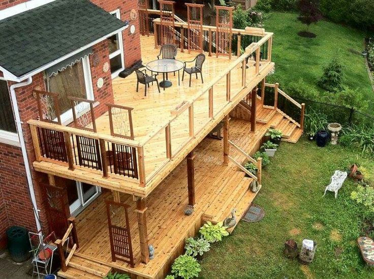 a large deck with chairs and tables in the middle of a garden area next to a brick building