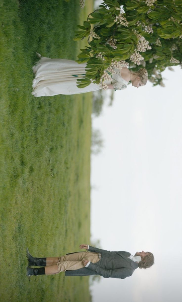 two people standing in the grass under a tree