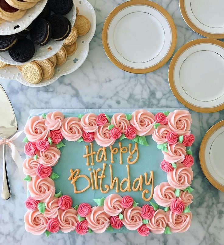 a birthday cake with pink frosting and roses on it, surrounded by plates and desserts