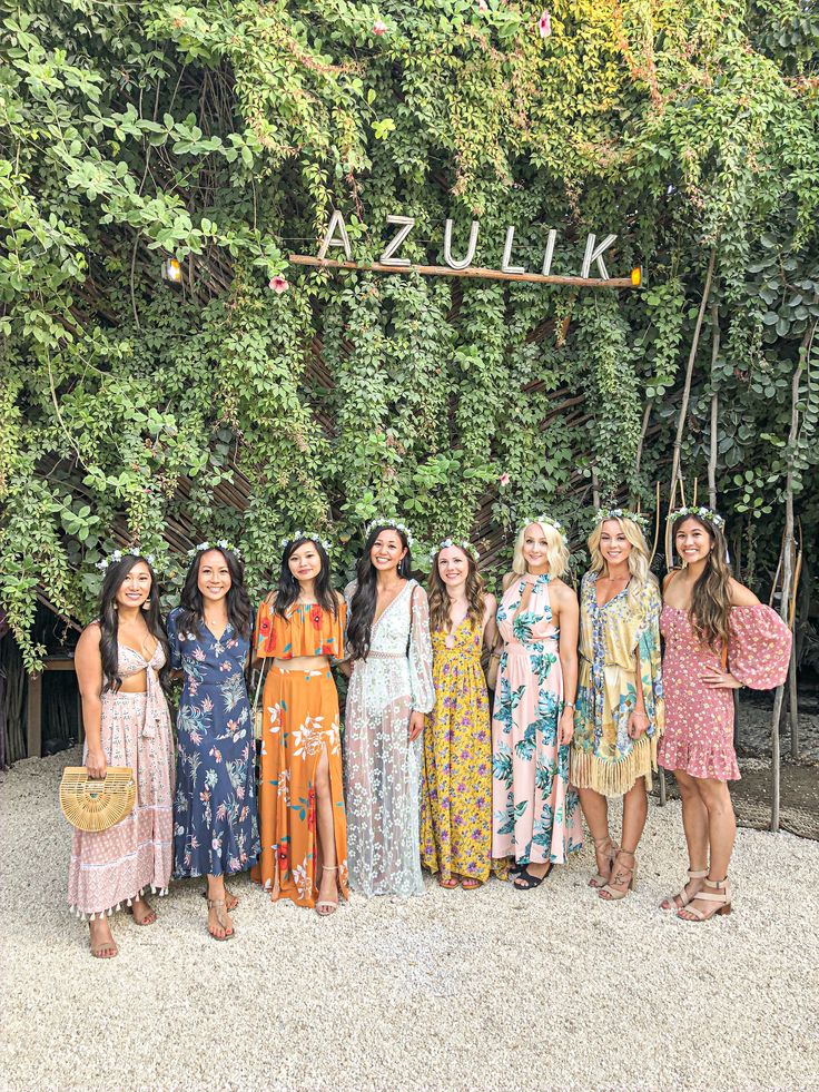 a group of women standing next to each other in front of a lush green wall