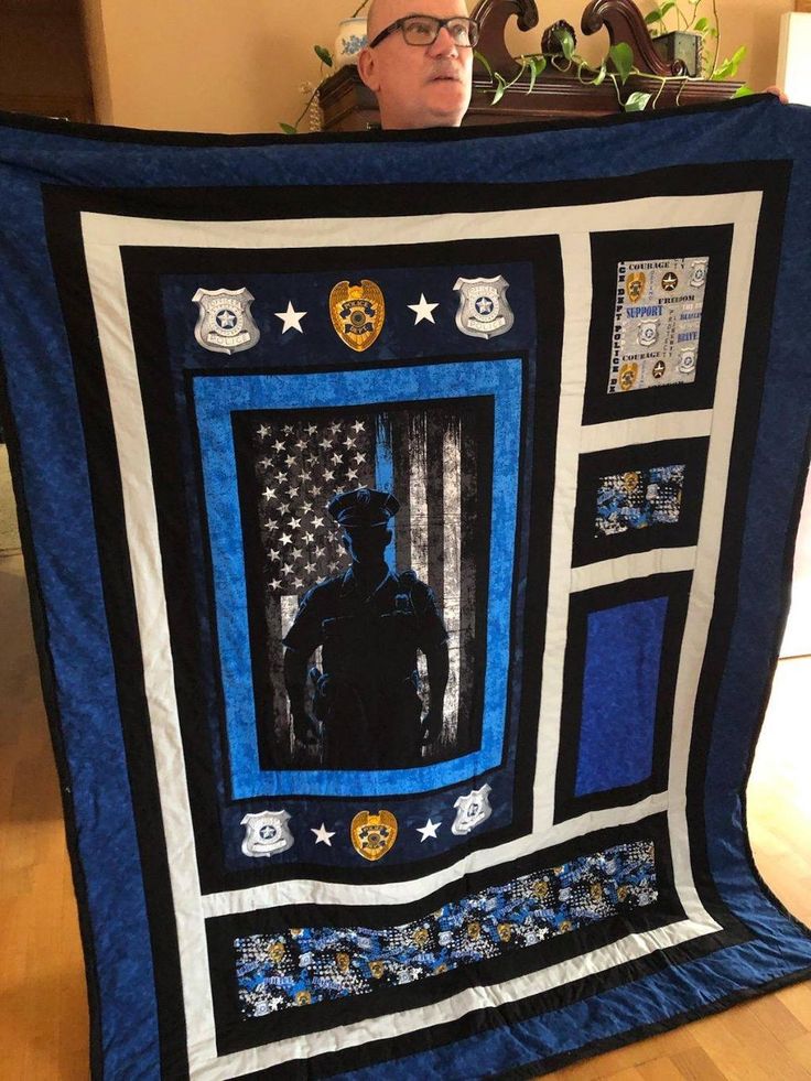 a man holding up a blue and black quilt with an image of a police officer on it